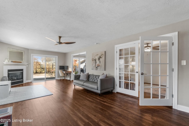 unfurnished living room with ceiling fan, a textured ceiling, a tile fireplace, dark wood-type flooring, and french doors