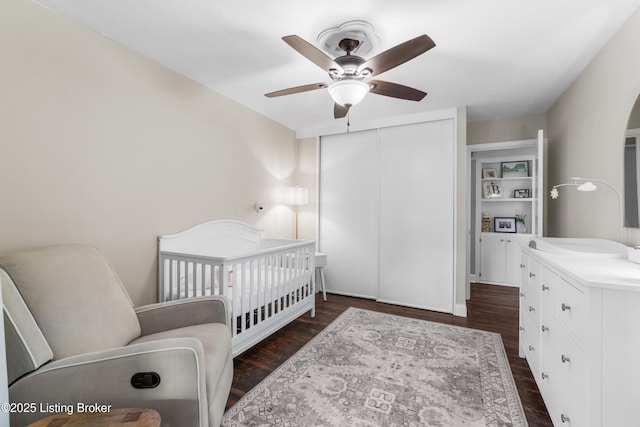 bedroom with ceiling fan, dark wood-style flooring, a closet, and a nursery area