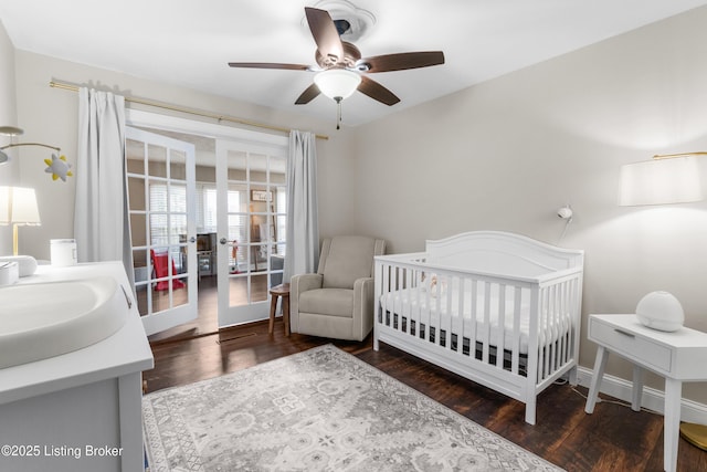 bedroom with dark wood-type flooring, a ceiling fan, a sink, a nursery area, and baseboards