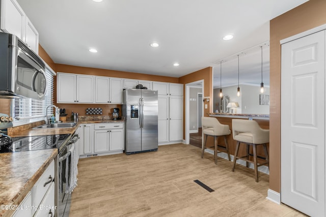 kitchen with a sink, visible vents, white cabinetry, hanging light fixtures, and appliances with stainless steel finishes