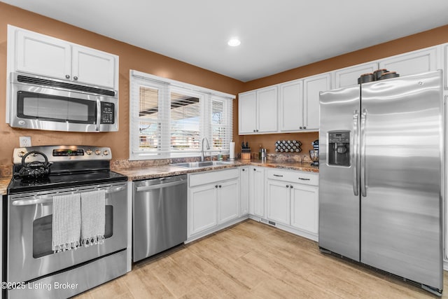 kitchen with dark stone counters, light wood-style flooring, stainless steel appliances, white cabinetry, and a sink