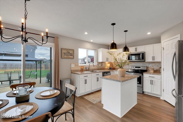 kitchen with wood finished floors, a kitchen island, a sink, white cabinets, and appliances with stainless steel finishes