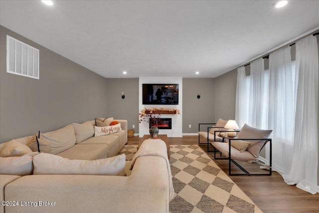 living room featuring wood finished floors, a glass covered fireplace, visible vents, and recessed lighting