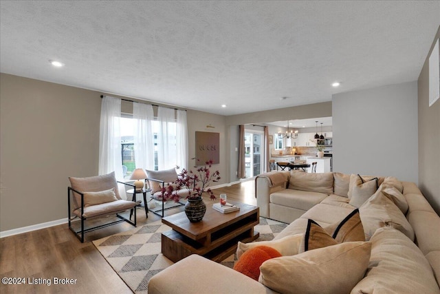 living room with baseboards, a textured ceiling, light wood finished floors, and an inviting chandelier