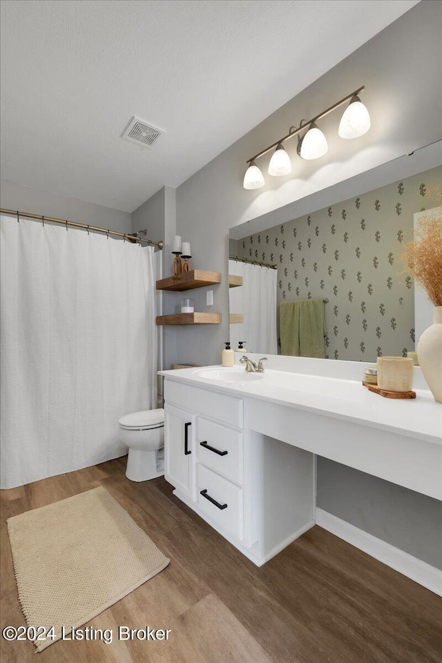 bathroom featuring toilet, wood finished floors, vanity, visible vents, and wallpapered walls