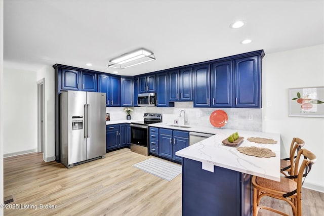 kitchen featuring light wood finished floors, appliances with stainless steel finishes, a sink, blue cabinets, and a peninsula