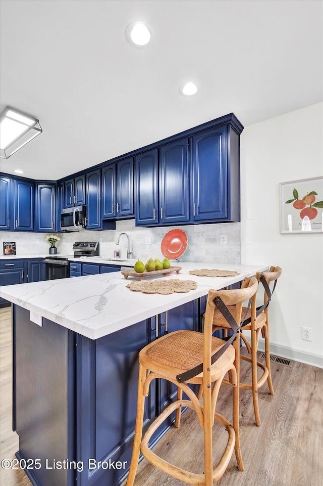 kitchen featuring stainless steel appliances, light wood-style flooring, blue cabinets, a peninsula, and a kitchen bar