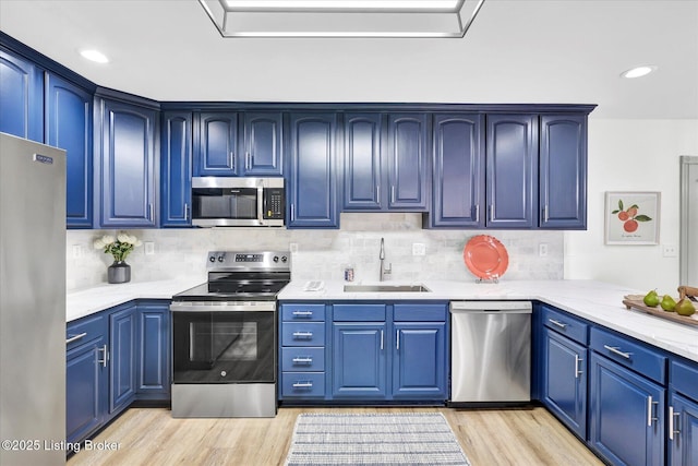 kitchen with blue cabinetry, stainless steel appliances, a sink, light stone countertops, and light wood-type flooring