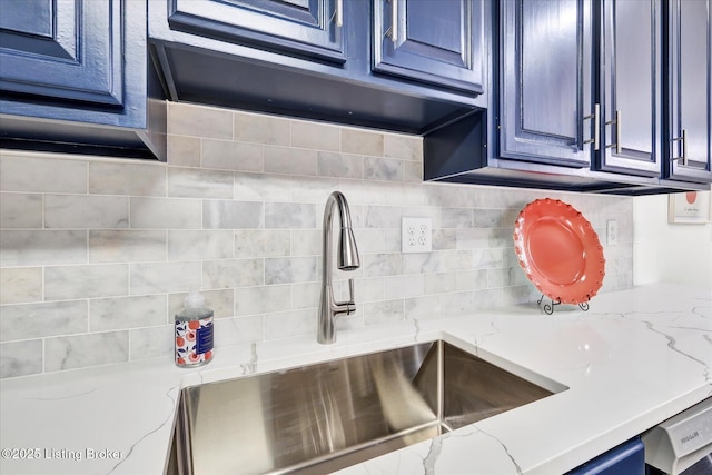 kitchen with blue cabinets, tasteful backsplash, light stone counters, and a sink