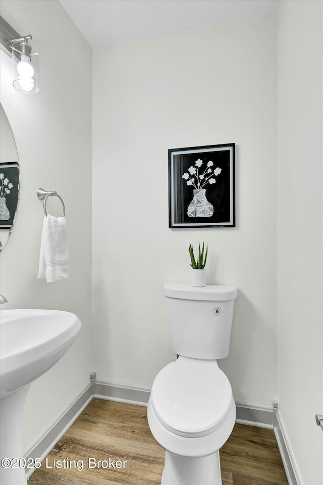 half bathroom with toilet, baseboards, and wood finished floors