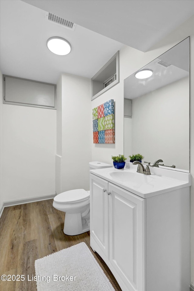 bathroom with toilet, wood finished floors, vanity, and visible vents