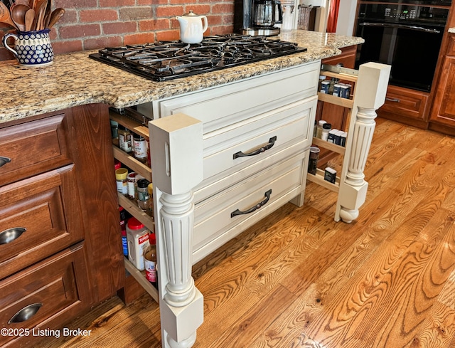 details with black appliances, light stone counters, decorative backsplash, and light wood finished floors