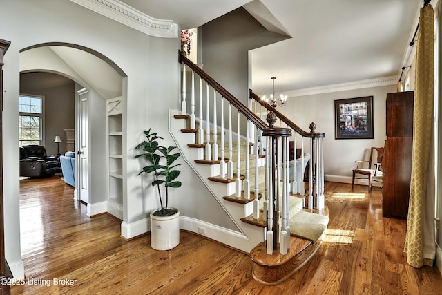 stairs with baseboards, arched walkways, wood finished floors, crown molding, and built in shelves