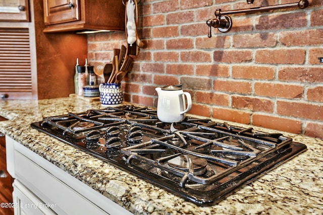 details featuring light stone counters, brown cabinets, black gas cooktop, and backsplash