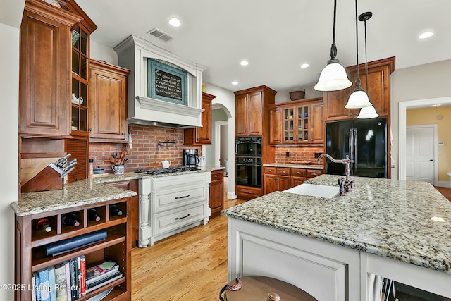 kitchen with arched walkways, a sink, visible vents, brown cabinets, and black appliances