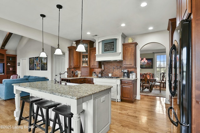 kitchen with arched walkways, decorative backsplash, light wood-style flooring, a kitchen breakfast bar, and freestanding refrigerator