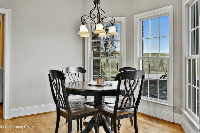 dining space featuring light wood finished floors, baseboards, visible vents, and a notable chandelier