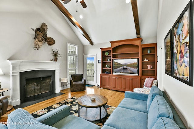 living area with vaulted ceiling with beams, light wood-style flooring, ceiling fan, and a fireplace with flush hearth