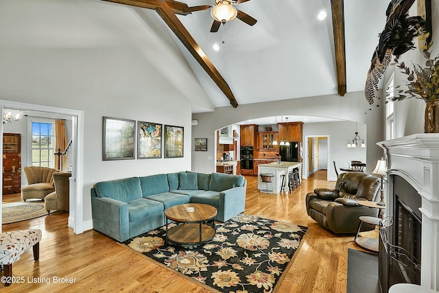 living area featuring arched walkways, beam ceiling, a fireplace, high vaulted ceiling, and light wood-type flooring