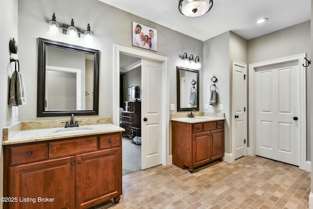 full bath with brick floor, two vanities, a sink, and baseboards