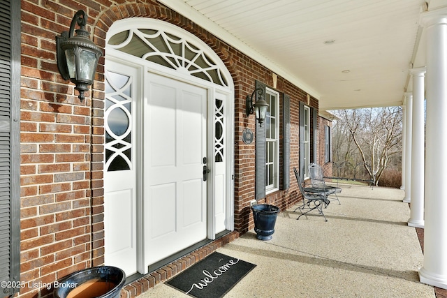 doorway to property featuring covered porch and brick siding