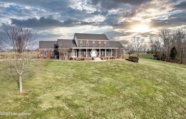 rear view of house with covered porch, brick siding, and a lawn