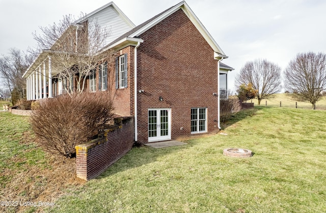 back of property featuring french doors, brick siding, a lawn, and an outdoor fire pit