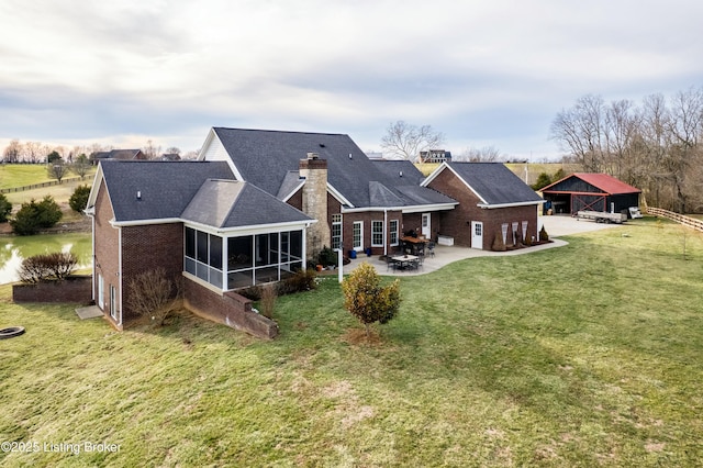 rear view of house with a sunroom, a chimney, a yard, a patio area, and brick siding