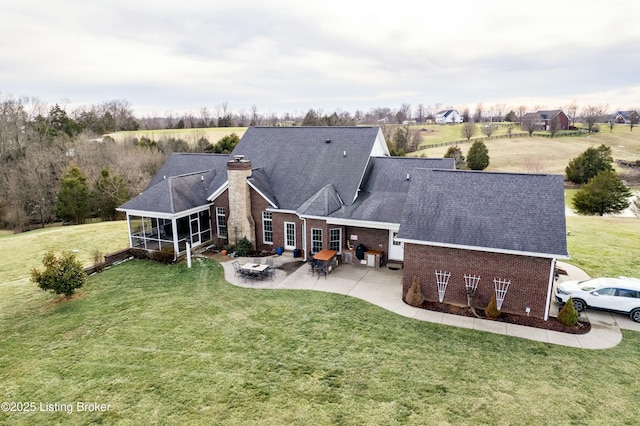 back of property featuring brick siding, a sunroom, a yard, a chimney, and a patio area