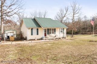 view of front facade with a shed, an outbuilding, metal roof, and a front yard