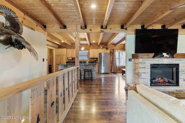 living area with wood ceiling, a stone fireplace, dark wood-style flooring, and beamed ceiling