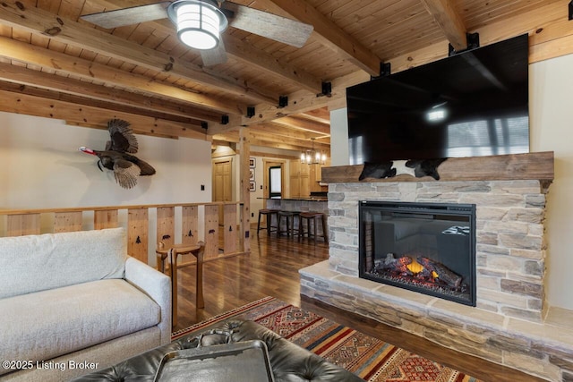 living area with a stone fireplace, wood finished floors, wood ceiling, a ceiling fan, and beamed ceiling