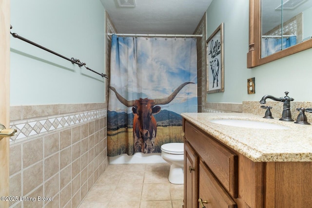 bathroom with a shower with shower curtain, toilet, tile patterned flooring, vanity, and tile walls