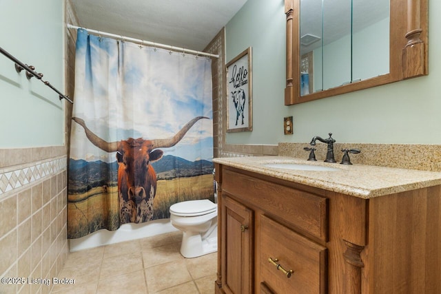 bathroom with toilet, tile walls, vanity, wainscoting, and tile patterned floors