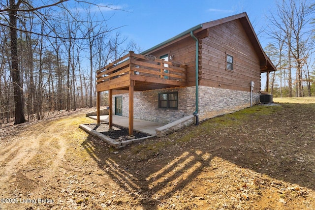 view of home's exterior with a deck, stone siding, a patio area, and cooling unit