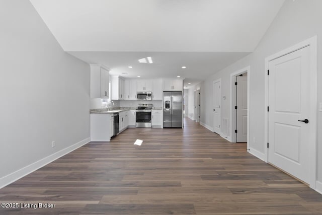 kitchen with dark wood-style flooring, appliances with stainless steel finishes, white cabinets, a sink, and baseboards