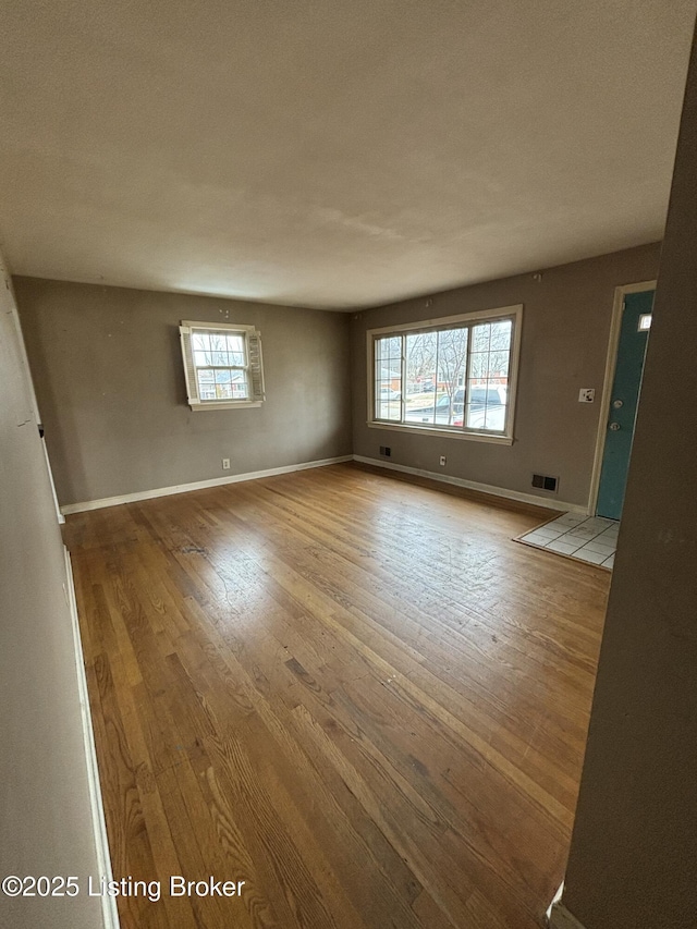 spare room with wood-type flooring, visible vents, and baseboards