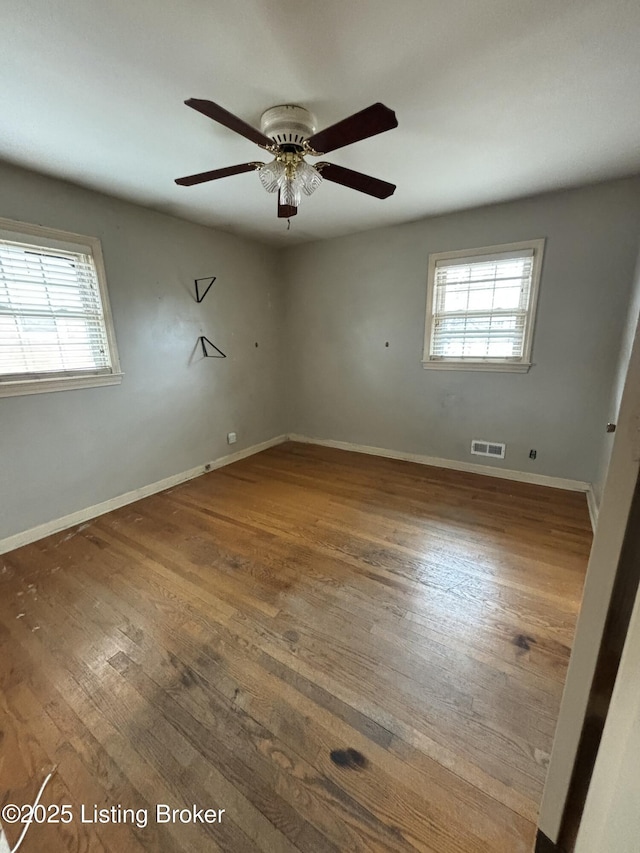 spare room featuring a ceiling fan, visible vents, baseboards, and hardwood / wood-style floors