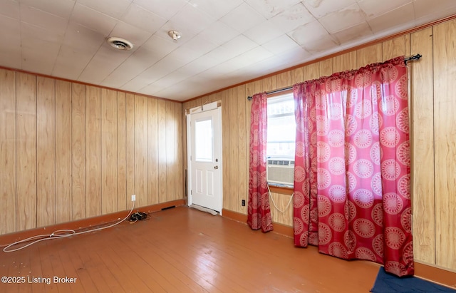 unfurnished room featuring cooling unit, hardwood / wood-style flooring, wood walls, visible vents, and baseboards