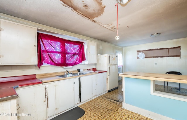 kitchen with light floors, light countertops, freestanding refrigerator, white cabinetry, and a sink