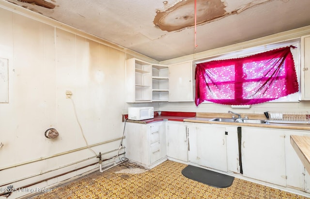 kitchen featuring white microwave, open shelves, a sink, white cabinets, and light floors