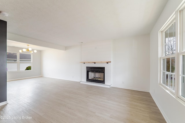 unfurnished living room with a large fireplace, baseboards, an inviting chandelier, a textured ceiling, and light wood-style floors