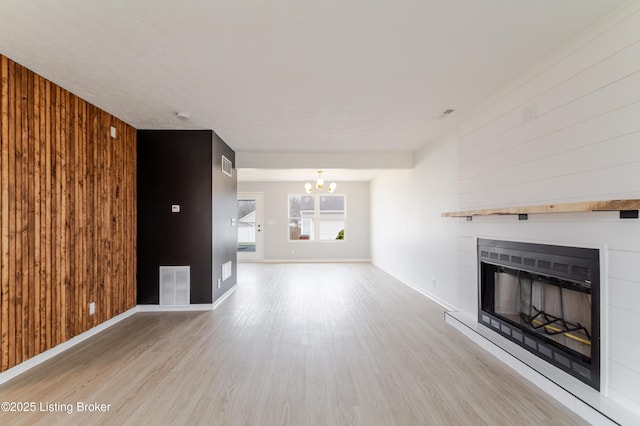 unfurnished living room with a glass covered fireplace, visible vents, wooden walls, and wood finished floors