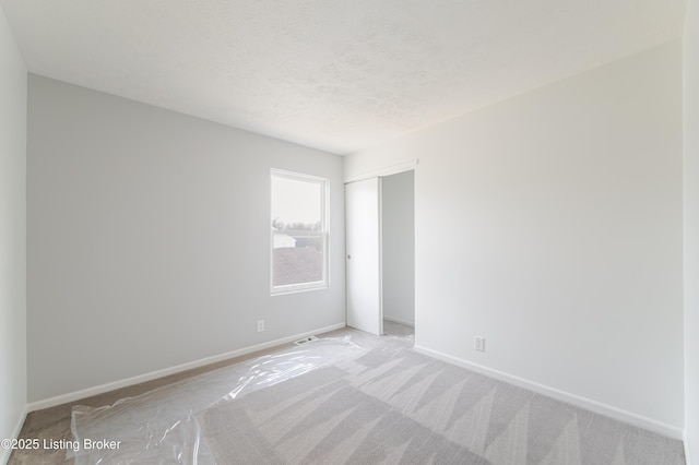 empty room with a textured ceiling, baseboards, visible vents, and light colored carpet