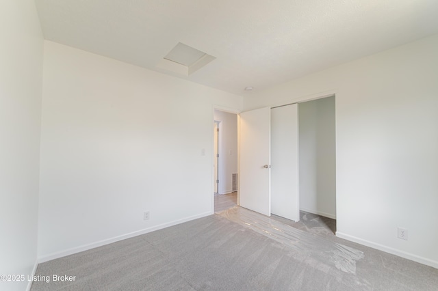 unfurnished bedroom featuring attic access, a closet, light colored carpet, and baseboards