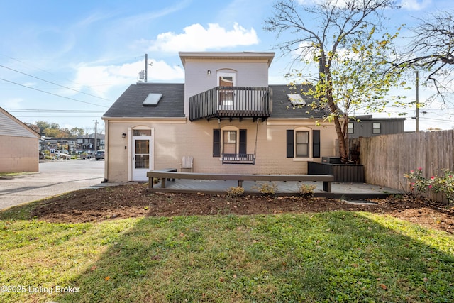 back of property featuring brick siding, fence, a balcony, and a lawn