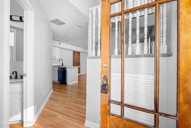 hall with baseboards, visible vents, a textured ceiling, light wood-style floors, and a sink