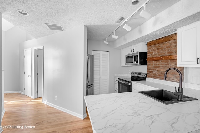 kitchen with a sink, visible vents, white cabinetry, light countertops, and appliances with stainless steel finishes