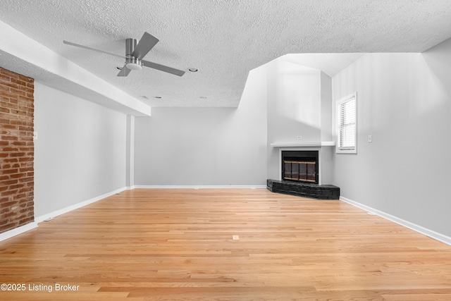 unfurnished living room with light wood finished floors, a glass covered fireplace, ceiling fan, a textured ceiling, and baseboards