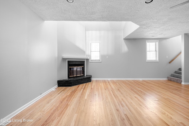 unfurnished living room featuring stairway, a glass covered fireplace, a textured ceiling, wood finished floors, and baseboards